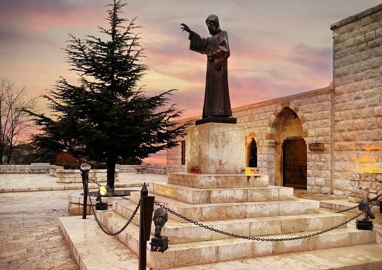 The bronze statue of St. Charbel in the monastery courtyard at dusk.
